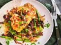 En tallrik med coq au vin blanc, kycklinglår med svamp, haricots verts och bacon i en ljus sås, garnerad med persilja.