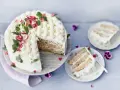 En vacker rabarberkompott tårta med flätmönster av grädde, garnerad med örter och blommor. En bit är upplagd på en tallrik.