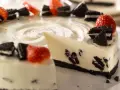 En krämig oreo cheesecake med färska jordgubbar och oreokex som dekoration. En bit är uppskuren.