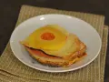 A toasted sandwich with melted cheese, ham, and a pineapple ring on top, served on a white plate.