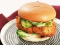 En saftig kyckling hamburgare med krispigt panerat kycklingfilé, gurka, jalapeños och en krämig sås på ett mjukt bröd. Serveras på en snygg tallrik.