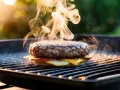 En saftig hamburgare med smält ost och tomat grillas. Röken stiger och indikerar perfekt hamburgare temperatur.