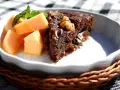 En bit saftig banankaka med choklad och nötter, serverad med färsk melon och mynta.