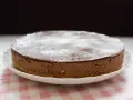 En krämig nutella cheesecake med chokladglasyr och pudersocker, serverad på en vit tallrik med en rosa rutig duk.