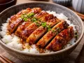 En skål med fluffigt ris toppad med saftig, glaserad teriyaki kyckling, garnerad med sesamfrön och grön lök.