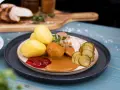 En tallrik med skivad ytterfile i sockerkaksform, potatis, sås, gelé och gurka.