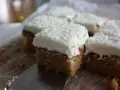 Färska bitar av morotskaka med krämig frosting och kokosflingor. En bit är uppskuren med en kniv.