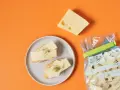 Slices of cheese on bread on a plate, a wedge of cheese, and a bag of cheese chunks.