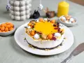 En vacker cheesecake påsk med gul topping, dekorerad med påskägg och nötter. Perfekt för påskfirandet!