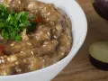 En krämig baba ganoush, toppad med färsk persilja och paprikapulver, bredvid skivade auberginer.