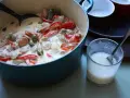 En krämig kreolsk gryta med korv, paprika, oliver och pickles i en blå gryta. En sked ligger i ett glas med mjölk.