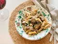 En tallrik med tryffelpasta med svamp och färska örter, serverad på en flätad duk. Ett glas rödvin står bredvid.