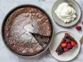 A whole chocolate cake with a slice removed, topped with powdered sugar, next to a slice of cake with berries and a dollop of whipped cream.