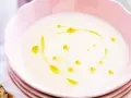 En krämig vit sparrissoppa med en virvel av olivolja i en rosa skål. Serveras med ett kryddigt bröd.