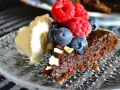 En bit nyttig kladdkaka med bär och grädde på ett mönstrat fat.