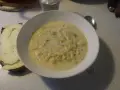 En krämig fänkålssoppa med potatis serveras i en vit skål, bredvid en bit rostat bröd med ost.