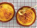 Två krämiga creme brulee i bruna skålar, en med en gyllene sked som lyfter fram den karamelliserade ytan.