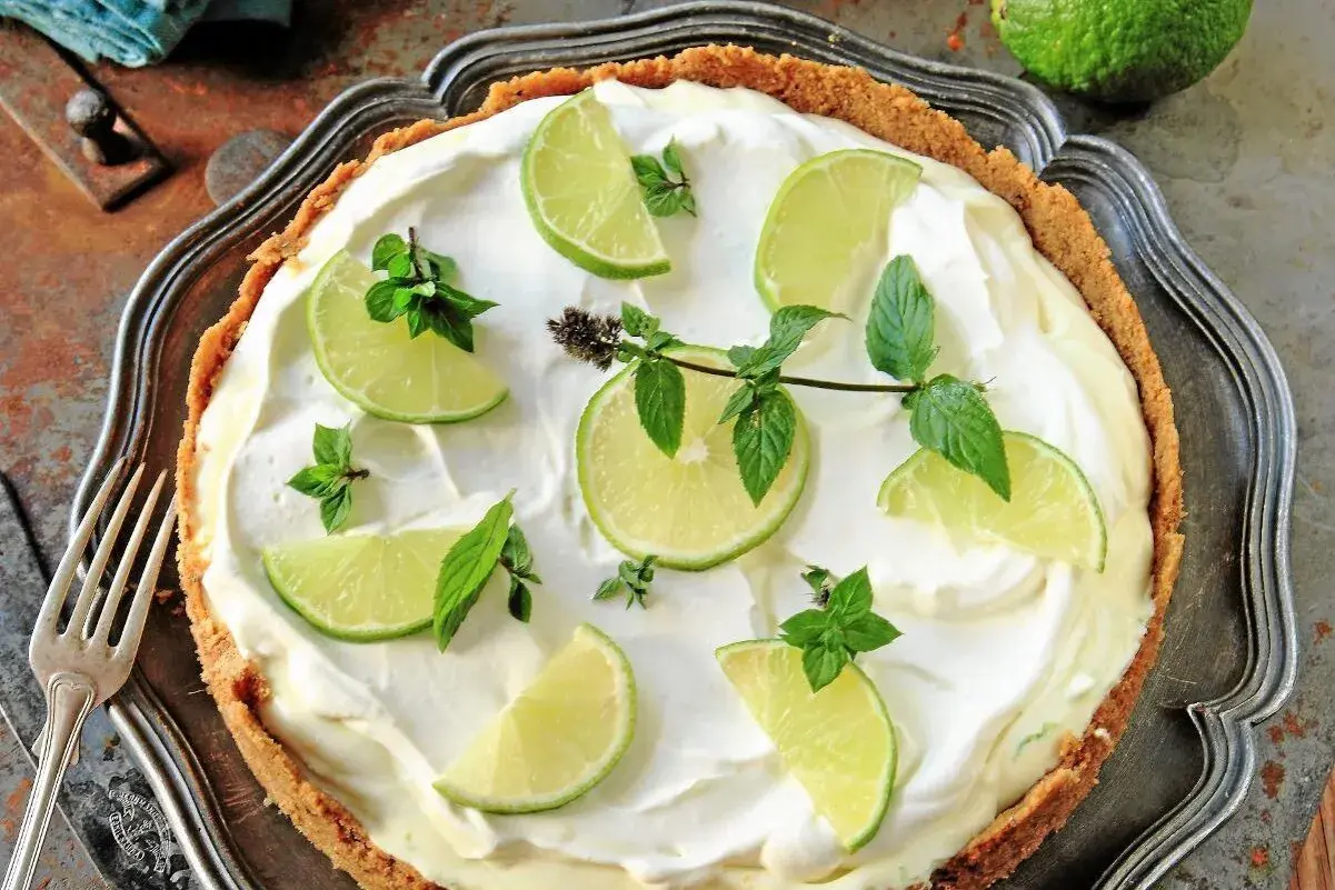 En krämig key lime pie med limeklyftor och mynta på en krispig botten, serverad på ett vackert fat.