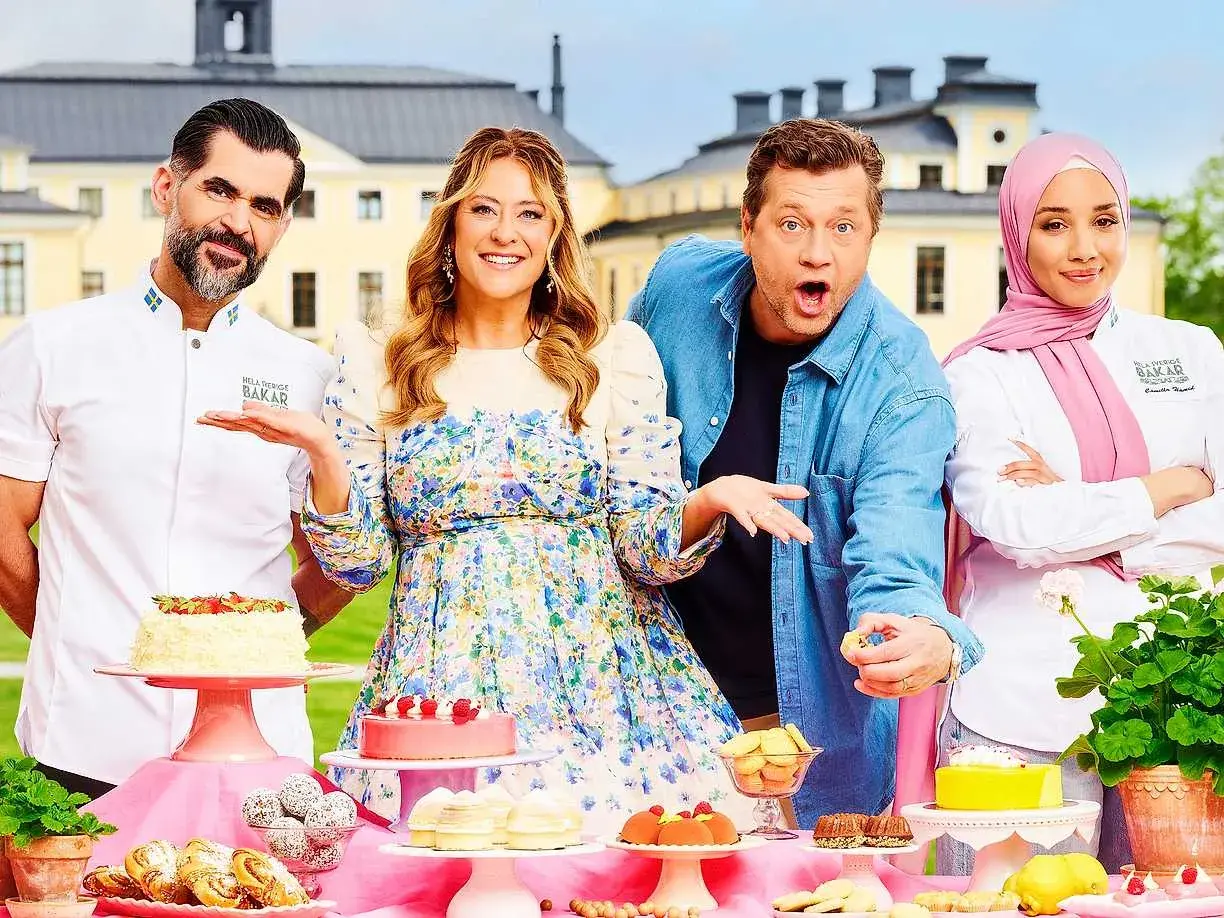 Fyra glada personer poserar vid ett bord fyllt med bakverk. De är med i Hela Sverige Bakar, redo att visa upp sina skapelser.