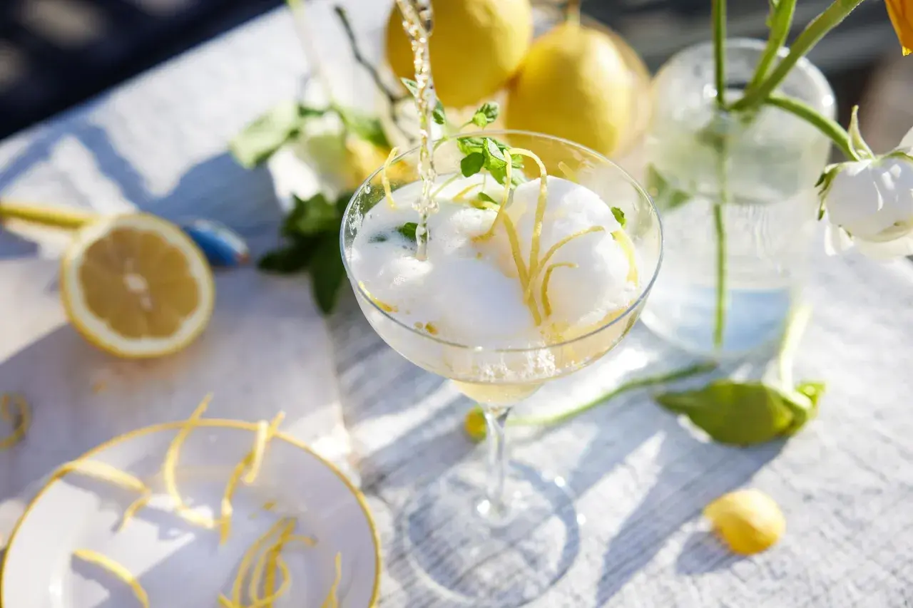 En bubblig drink med citronskal och mynta hälls upp i ett glas. Perfekt att bjuda på fika till många.