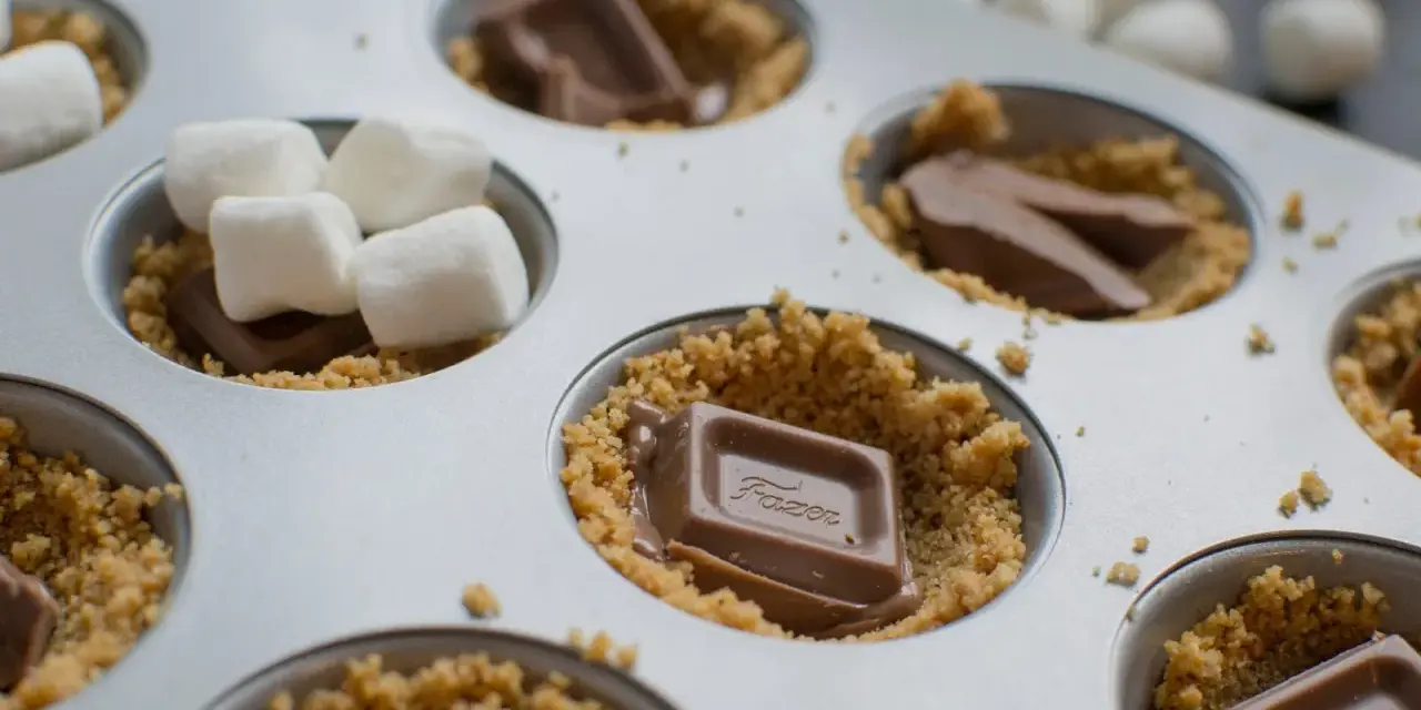 S'mores i ugn förbereds i en muffinsform med krossade kex, chokladbitar och marshmallows.