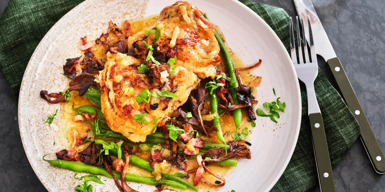 En tallrik med coq au vin blanc, kycklinglår med svamp, haricots verts och bacon i en ljus sås, garnerad med persilja.