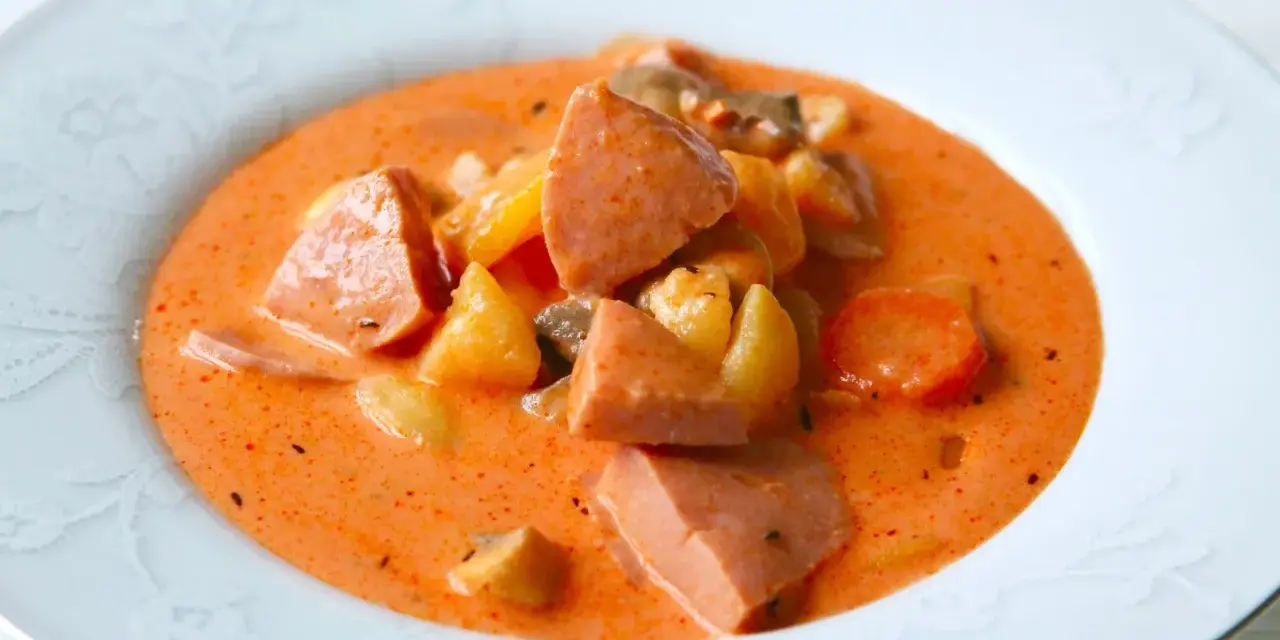 A hearty bowl of korvsoppa with sausage, potatoes, and carrots in a creamy orange broth.