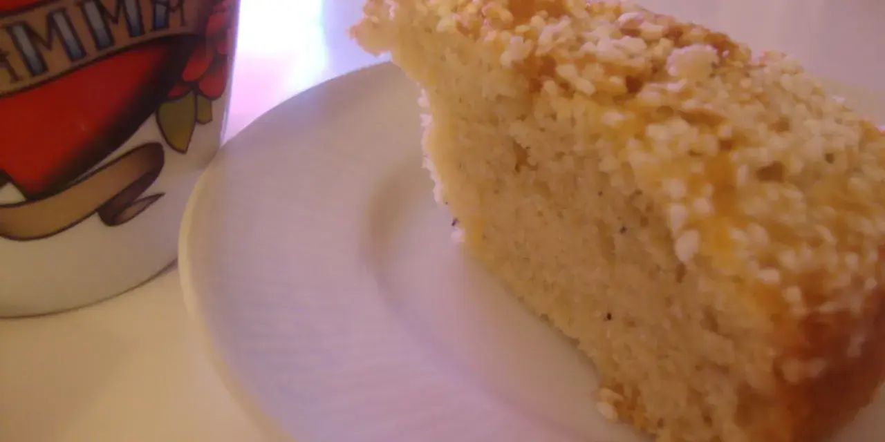 En bit saftig sockerkaka med kardemumma, toppad med nötter, ligger på en vit tallrik bredvid en mugg med texten "MAMMA".