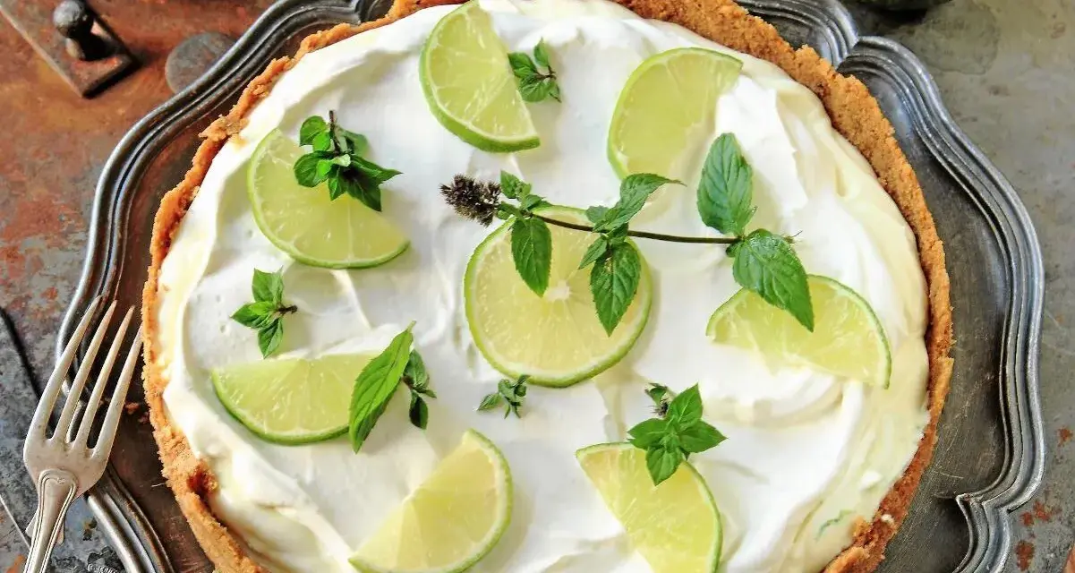 En krämig key lime pie med limeklyftor och mynta på en krispig botten, serverad på ett vackert fat.