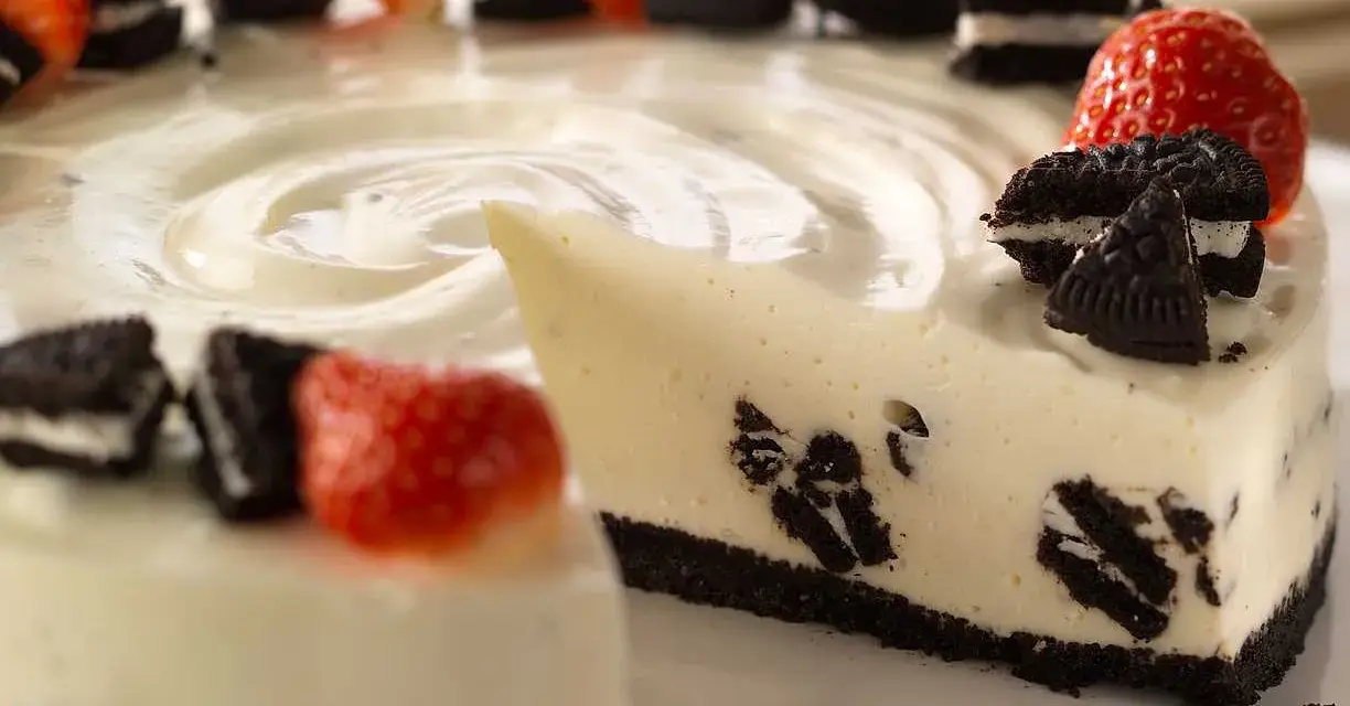 En krämig oreo cheesecake med färska jordgubbar och oreokex som dekoration. En bit är uppskuren.