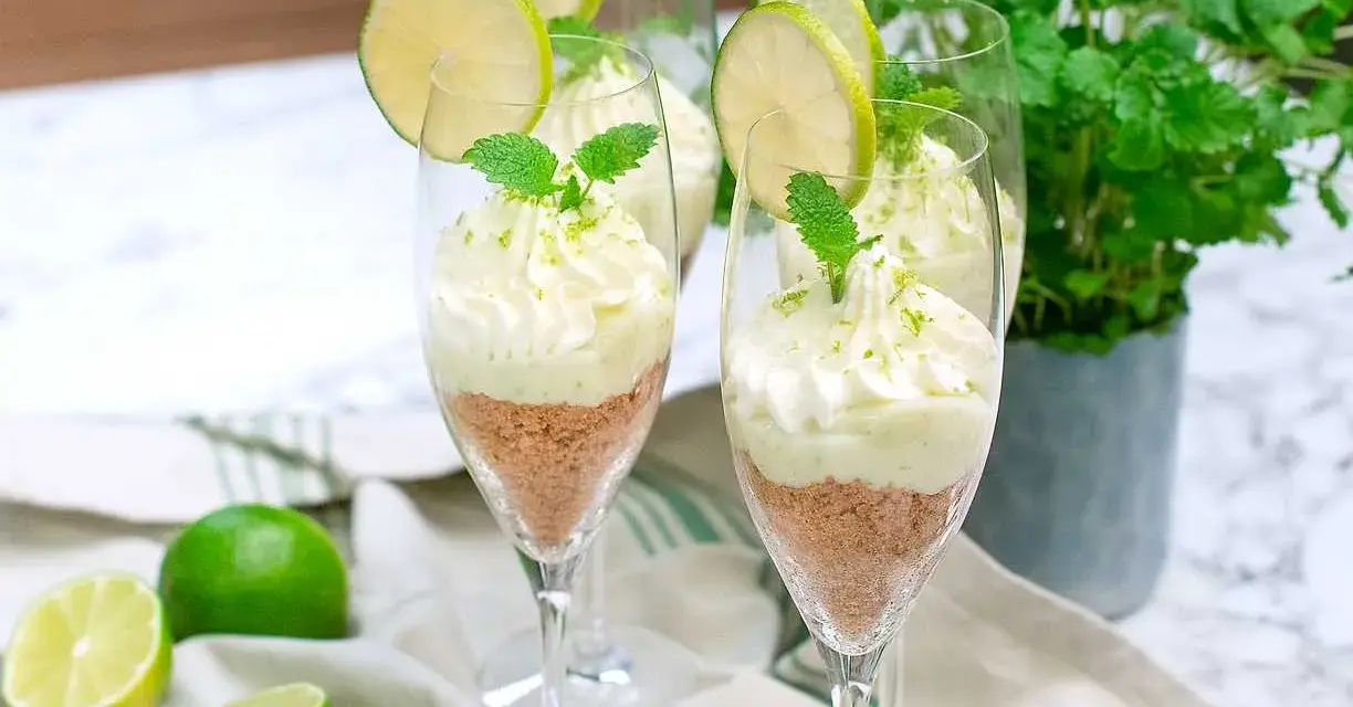 Key lime pie in glasses with whipped cream, lime slices, and mint.