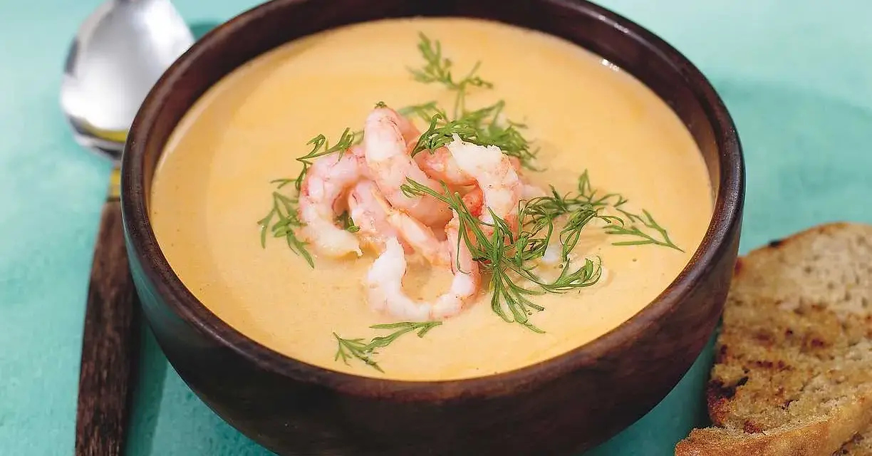 En krämig soppa med räkor och dill, serverad i en träskål med rostat bröd. En härlig soppa med räkor som värmer.