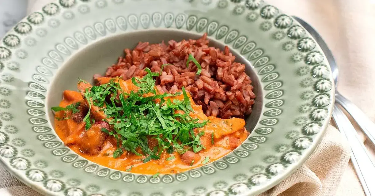 En portion korv stroganoff med rött ris, toppad med färsk persilja, serveras på en vacker grön tallrik.