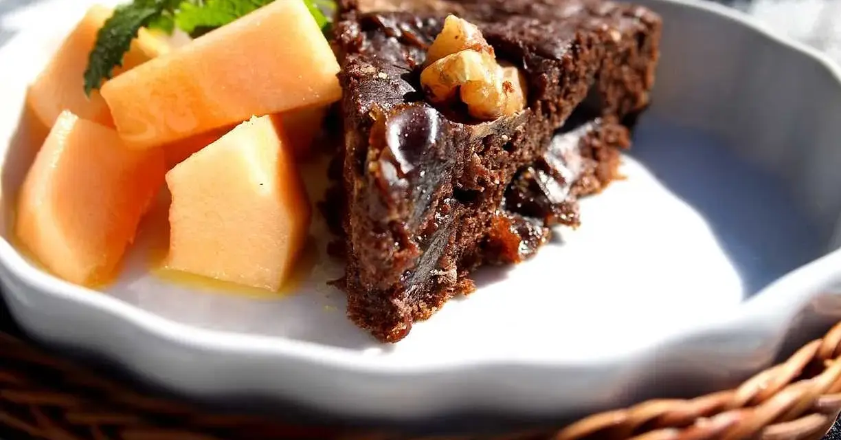 En bit saftig banankaka med choklad och nötter, serverad med färsk melon och mynta.