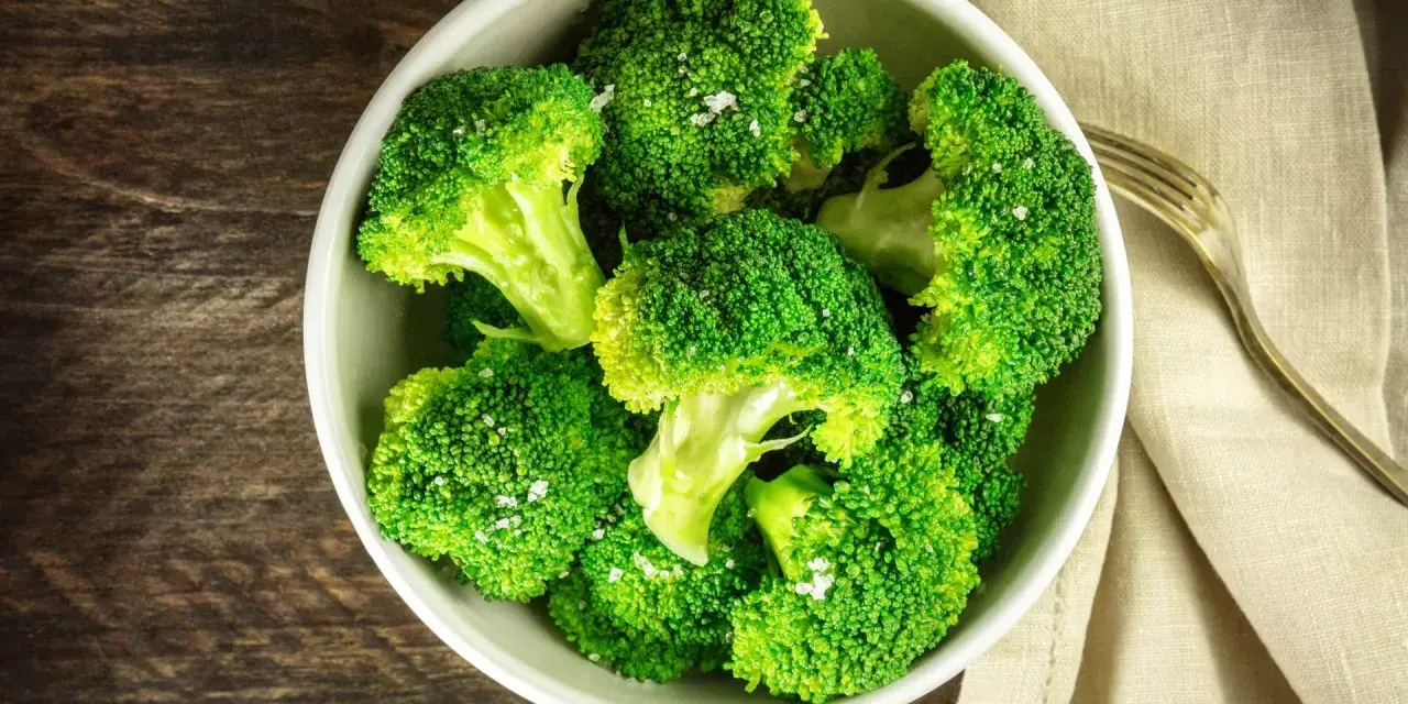 En skål med nykokt, grön broccoli, strödd med flingsalt. En gaffel ligger bredvid på en beige duk.