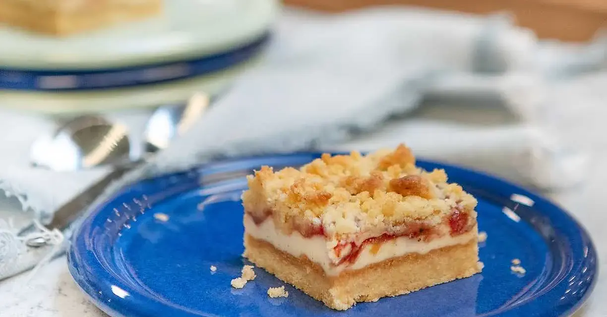 A slice of rhubarb cheesecake with a crumb topping on a blue plate.