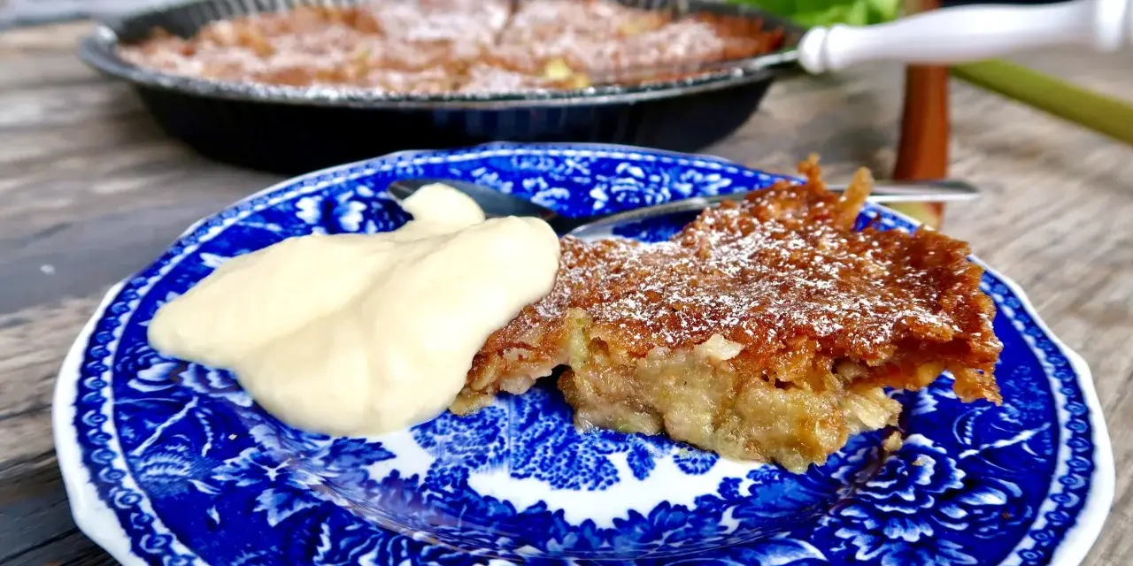 A slice of rhubarb pie with a dollop of cream on a blue and white patterned plate.