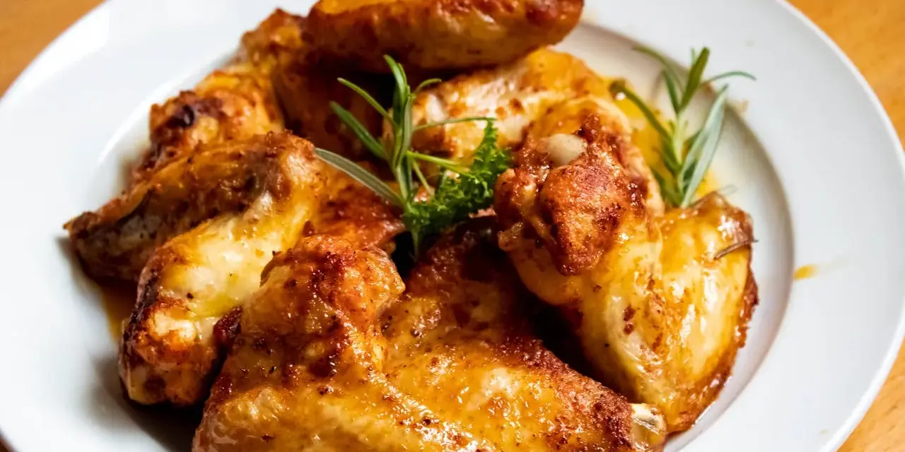 En tallrik med gyllene, grillade kycklingvingar, garnerade med rosmarin. Perfekt för en festmåltid, och med rätt förvaring har grillad kyckling hållbarhet som räcker för att njuta av resterna.