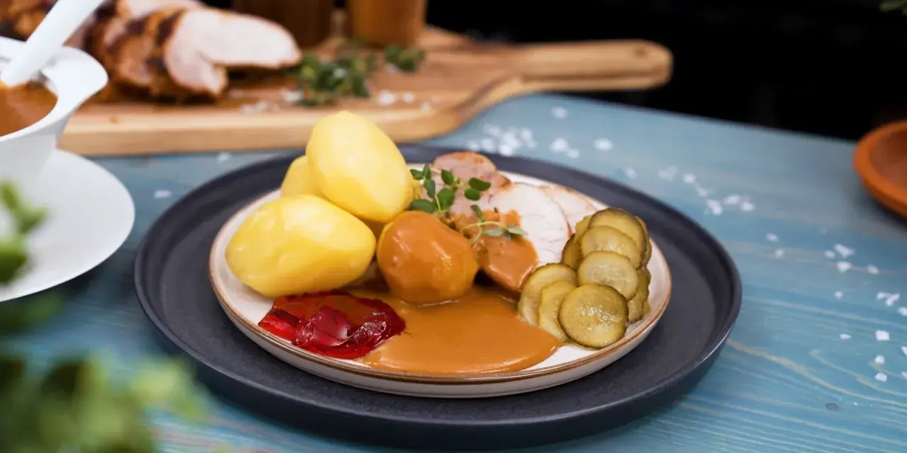 En tallrik med skivad ytterfile i sockerkaksform, potatis, sås, gelé och gurka.