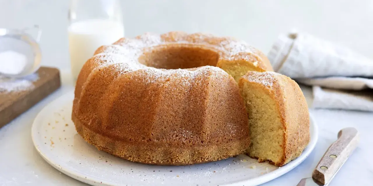 A golden-brown bundt cake dusted with powdered sugar, with a slice removed.