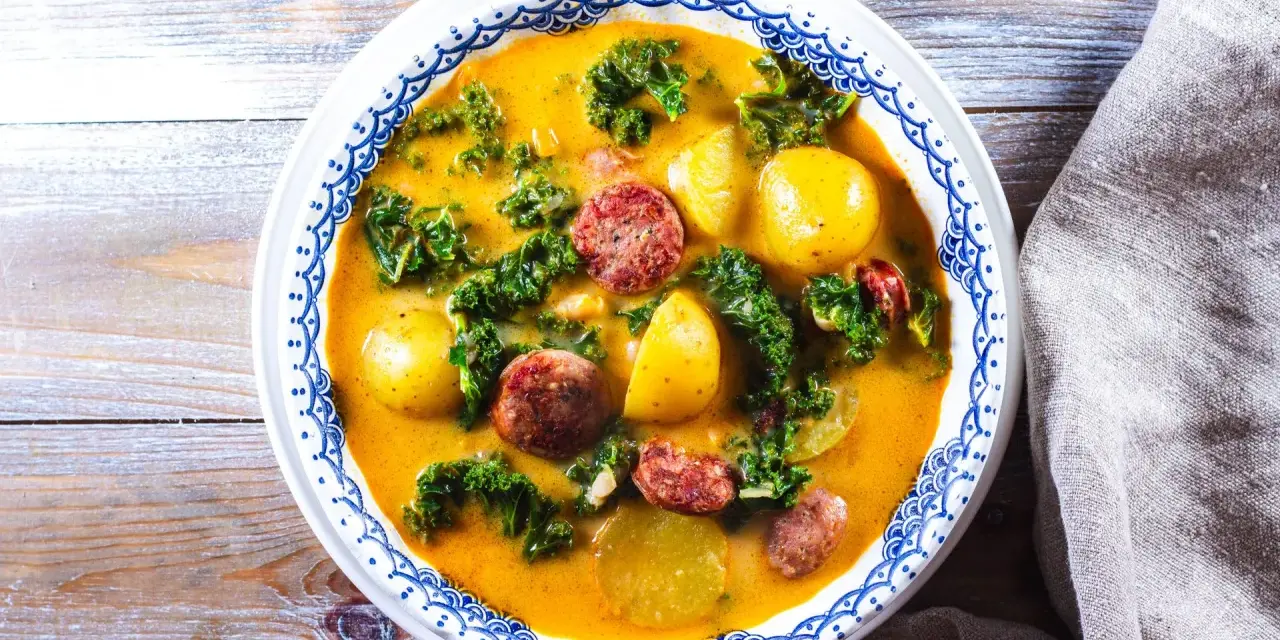 En mustig grönsakssoppa med potatis, grönkål och korvskivor i en gul buljong.