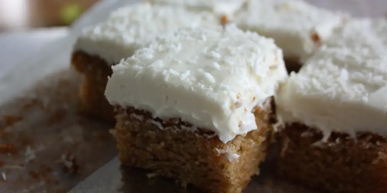 Färska bitar av morotskaka med krämig frosting och kokosflingor. En bit är uppskuren med en kniv.