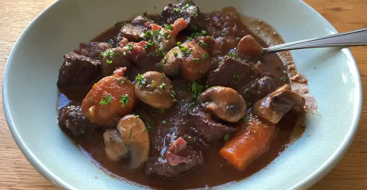 En skål med mustig boeuf bourguignon, fylld med mört kött, champinjoner och morötter, toppad med persilja.