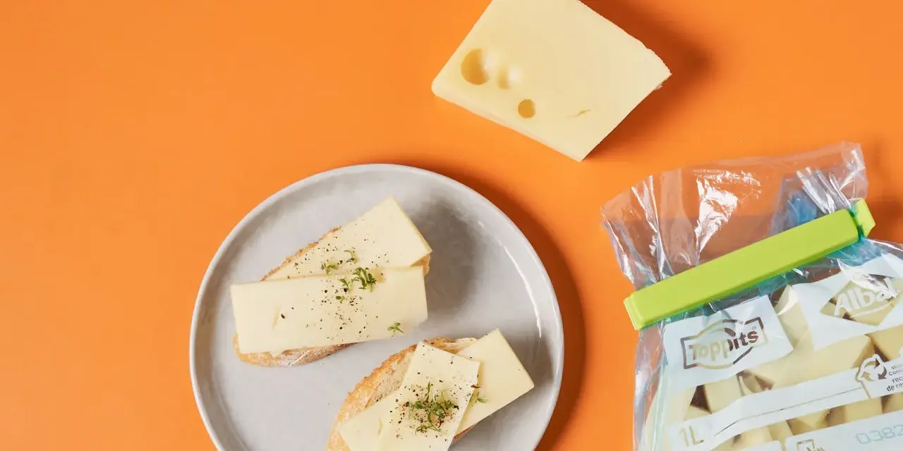 Slices of cheese on bread on a plate, a wedge of cheese, and a bag of cheese chunks.