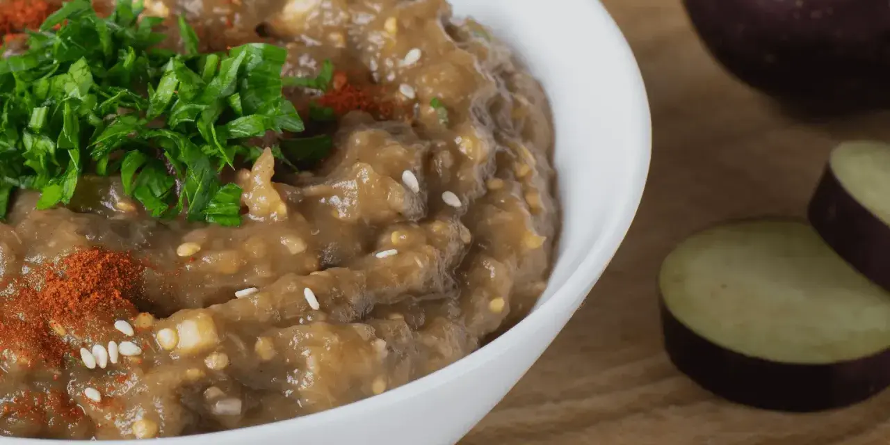 En krämig baba ganoush, toppad med färsk persilja och paprikapulver, bredvid skivade auberginer.