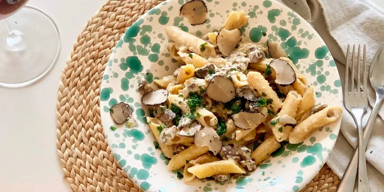 En tallrik med tryffelpasta med svamp och färska örter, serverad på en flätad duk. Ett glas rödvin står bredvid.
