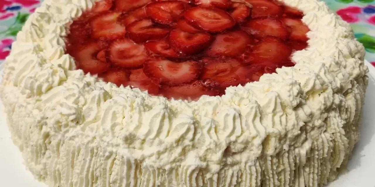 A round cake with whipped cream frosting and sliced strawberries on top.