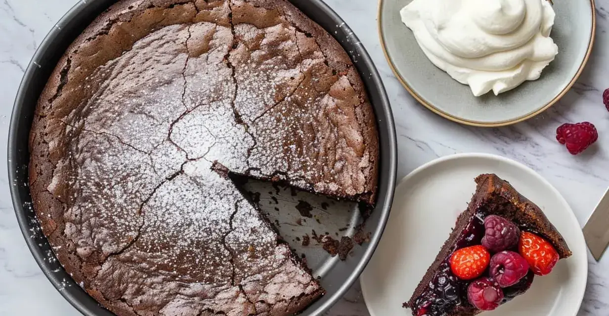 A whole chocolate cake with a slice removed, topped with powdered sugar, next to a slice of cake with berries and a dollop of whipped cream.
