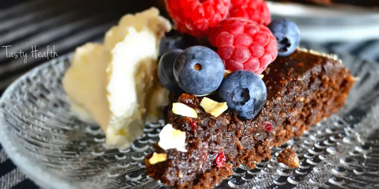 En bit nyttig kladdkaka med bär och grädde på ett mönstrat fat.
