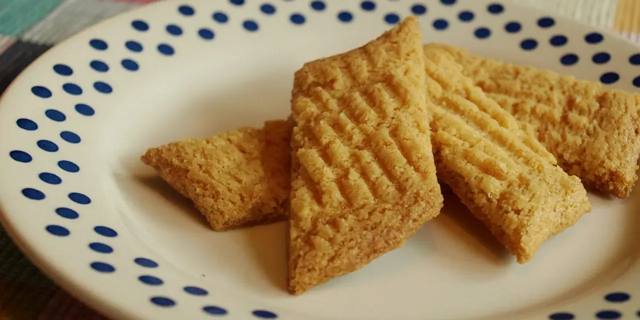 Tre gyllene glutenfria kolakakor ligger på en vit tallrik med blå prickar. De har ett rutmönster på ovansidan.